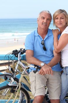 A middle aged couple biking by the seashore.