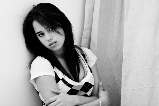 black and white portrait of a young woman leaning against a wall hugging herself