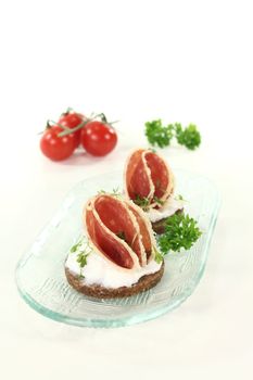 Pumpernickel bread with cream cheese, salami and garden cress on a glass bowl