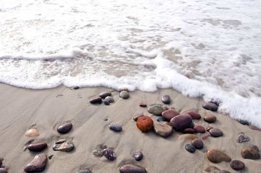 Sea waves beating stones lying in sea sand on coast line.