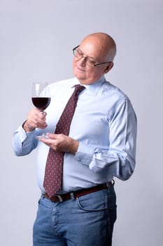 portrait of a successful senior man with glass of wine on gray background