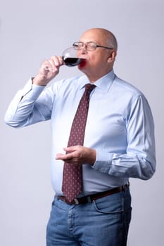 portrait of a successful senior man with glass of wine on gray background