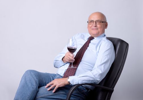 portrait of a successful senior man with glass of wine on gray background