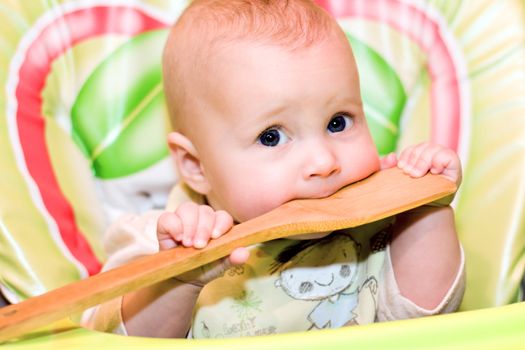 baby biting a wooden spoon on a colourful background