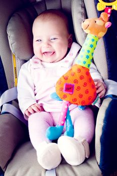 smiling baby girl in green car seat with her toy