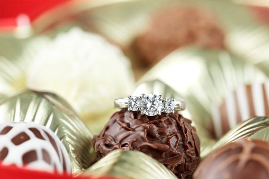 Diamond engagement inside of a box of chocolate truffles. Extreme shallow depth of field with selective focus on diamond ring. 