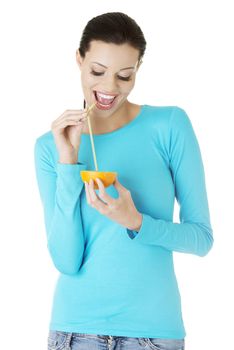 Attractive smiling young woman drinking orange juice straight from fruit