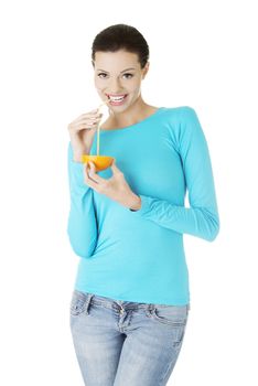 Attractive smiling young woman drinking orange juice straight from fruit