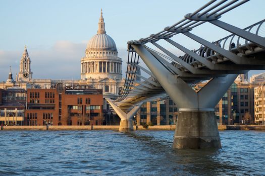 The iconic view of London - the famous pedestrian Millennium Bridge over the Thames with views of St. Paul's Cathedral in the warm rays of the setting sun
