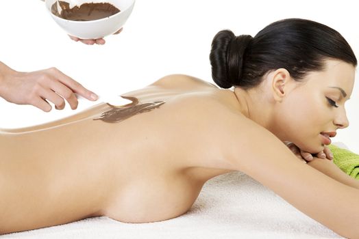 Pretty young woman relaxing being massaged in spa saloon with chocolate. Isoalted on white