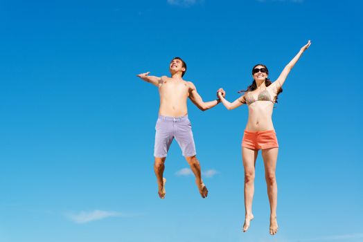 young couple jumping together on a blue sky background