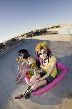 Fisheye shot of girls in brightly colored clothing in a plastic pool on a roof with sunglasses and lollipops