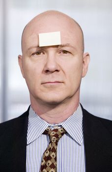 Bald businessman in with a blank sticky note on his forehead