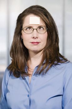 Businesswoman in a blue shirt with a blank sticky note on her forehead