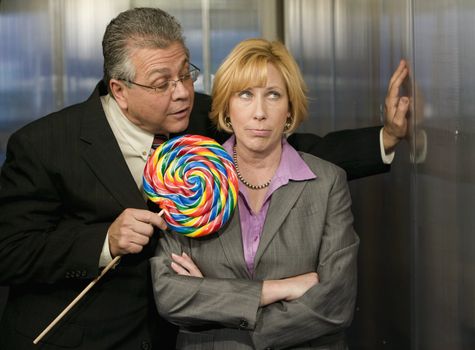 Man tempts woman with a big lollipop in an office