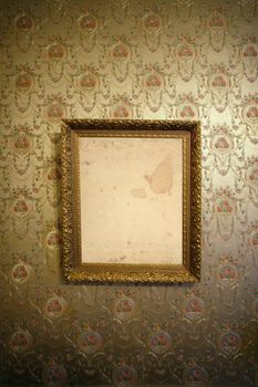 Photo of an antique frame hanging on a wall with vintage wallpaper.