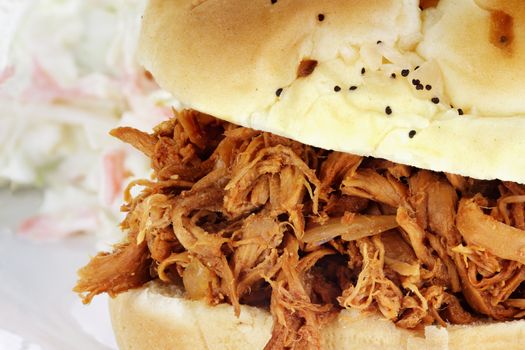 Close up of pulled chicken sandwich with coleslaw in the background. 
