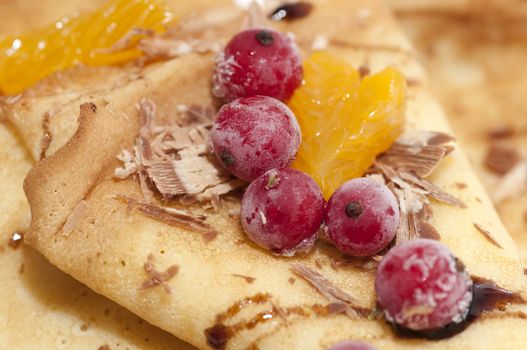 Pancakes with orange, shaving chocolate and red currants close up