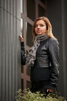 Beautiful girl in autumn coat standing near expensive granite facade. Wind waving her hair beautifully. girl smiling