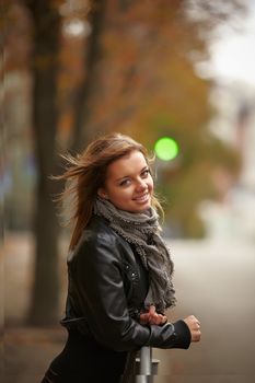 Beautiful girl in autumn city. Standing, leaning on a fence on the background of the green light