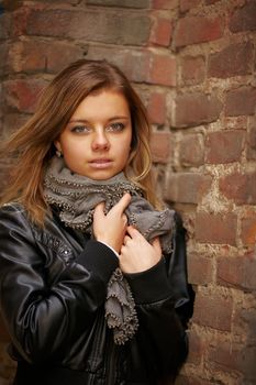 Beautiful girl in autumn coat standing near red brick wall. Presses his hands to his chest jacket.