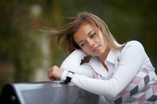 Beautiful girl thoughtfully sitting on the bench in autumn park