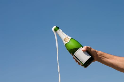 Hand holding an open bottle of champagne on a background of the blue sky