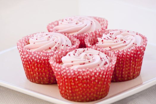A plate of frosted strawberry cupcakes in red and white cases