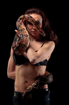 Mysterious beautiful exotic woman with a boa entwined around her body standing in shadows on a dark background