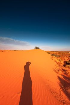 Photographer shadow on Red outback ripple sand dune desert with blue sky.