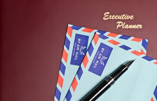 a dark red executive planner with two blue color envelopes and pens in landscape orientation