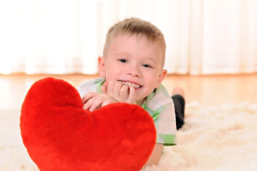 the child is lie on the floor with a red plush heart