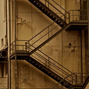 Fire escape stairs on the side of a weathered building in sepia