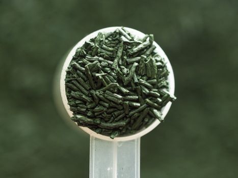 closeup of dry spirulina flakes with a measuring spoon used as food supplement rich of vitamins, antioxidants and minerals