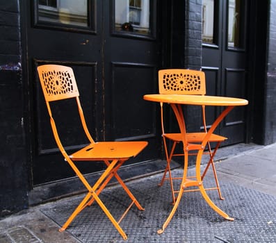 Two orange chairs and a orange table on the sidewalk