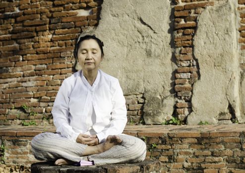 Buddhist woman meditating against ancient temple