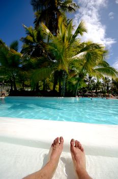 A man has his bare feet in a the water of a swimming pool.