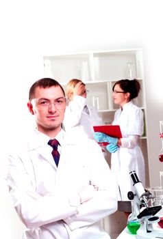 Three doctors are smiling at the camera in a doctors' office. Horizontally framed shot.