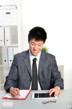 Smiling Asian business man taking notes and looking at tablet