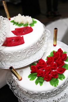 Decorated two tiered wedding cake with red and white roses on display at a reception, high angle view