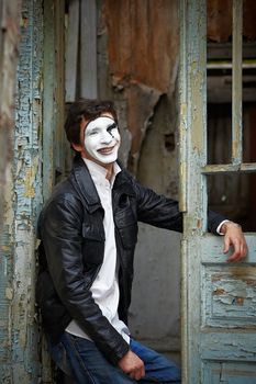 Guy mime against the old wooden door. Mime sits in the doorway and smiled sarcastically