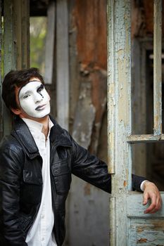 Guy mime against the old wooden door. Mime sits in the doorway and smiled sarcastically