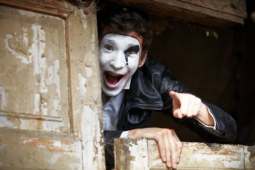 Portrait of a Man ​​mime. Grimacing near the old wooden door with peeling paint. Point the finger at the camera