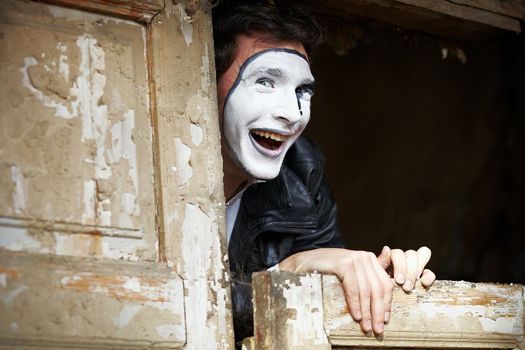 Portrait of a Man ​​mime. Grimacing near the old wooden door with peeling paint. Cocked his head