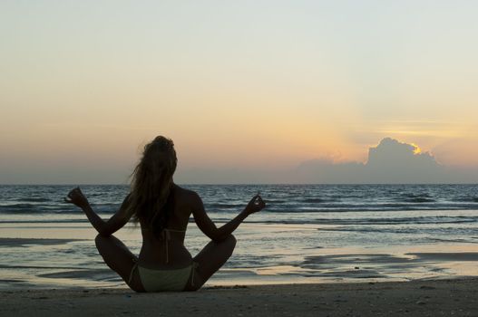 Meditating woman on the sand beach at sunset background in India, Goa