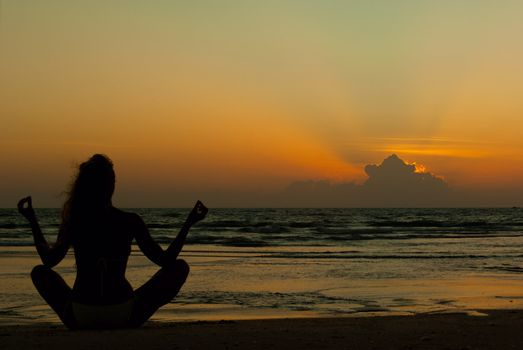 Silhouette of a woman meditating by the sea on sunset