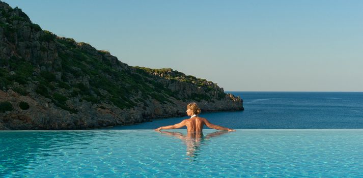 Beautiful woman relaxing in infinity swimming pool near coast 