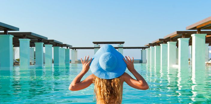 Beautiful blonde woman relaxing near extraordinary pool in sunny day