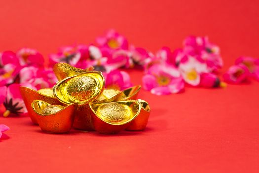 Golden Chinese New Year Ingots on red surface with plum blossoms in background