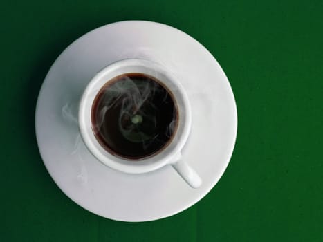 White cup of hot coffee on green table